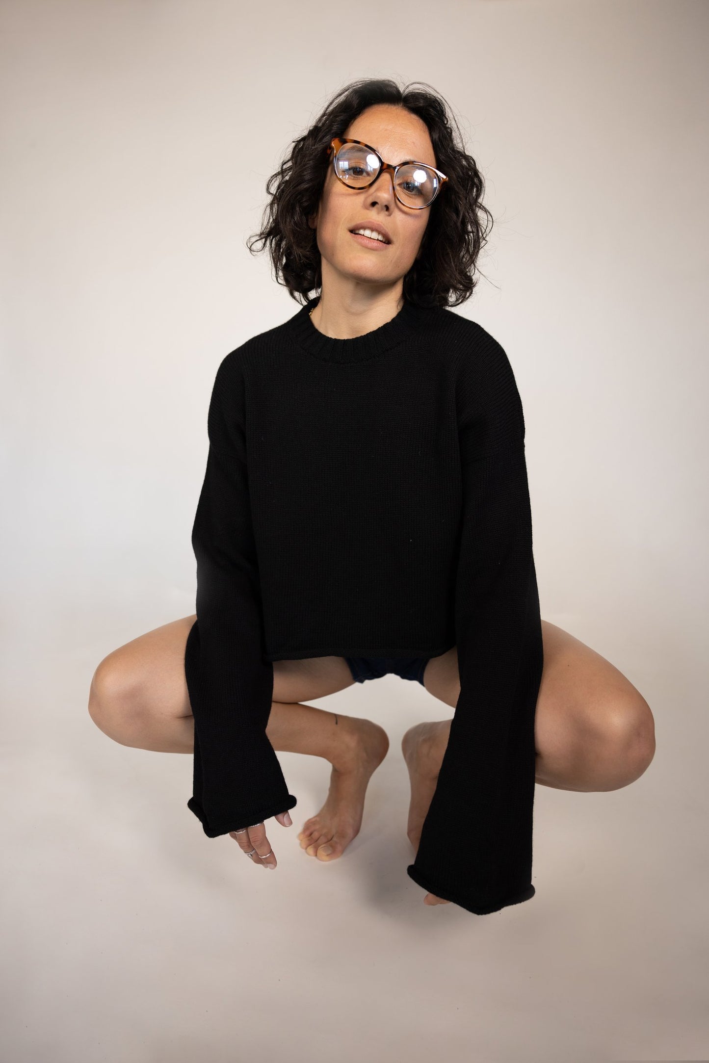 Person wearing a black jacket over a red bikini top and blue jeans, standing against a neutral background.
givéh knitwear handmade by female artisans in iran using only natural and recycled fibres. contemporary knitwear for cool people. crewneck backless sweater in black. 100% merino wool. fall 2025 collection.