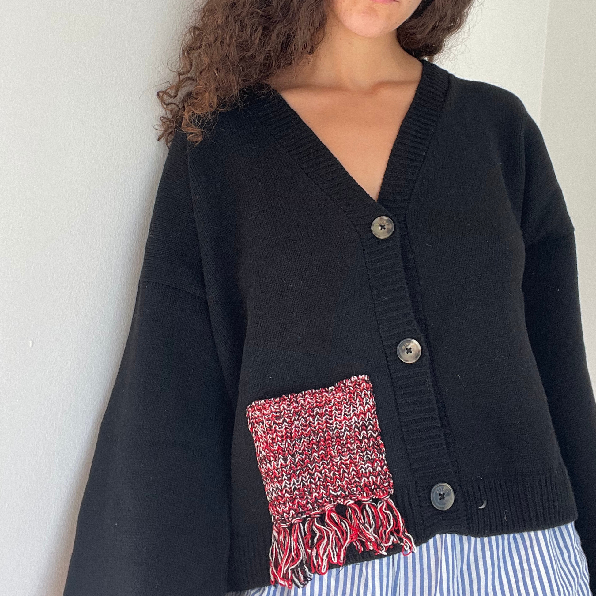 Person wearing a black cardigan with a red and black patterned pocket on a white background.
givéh knitwear handmade by female artisans in iran using only natural and recycled fibres. contemporary knitwear for cool people. black cardigan with red/black gradient fringe pocket. 3 natural horn buttons. 100% merino wool. fall 2025 collection.