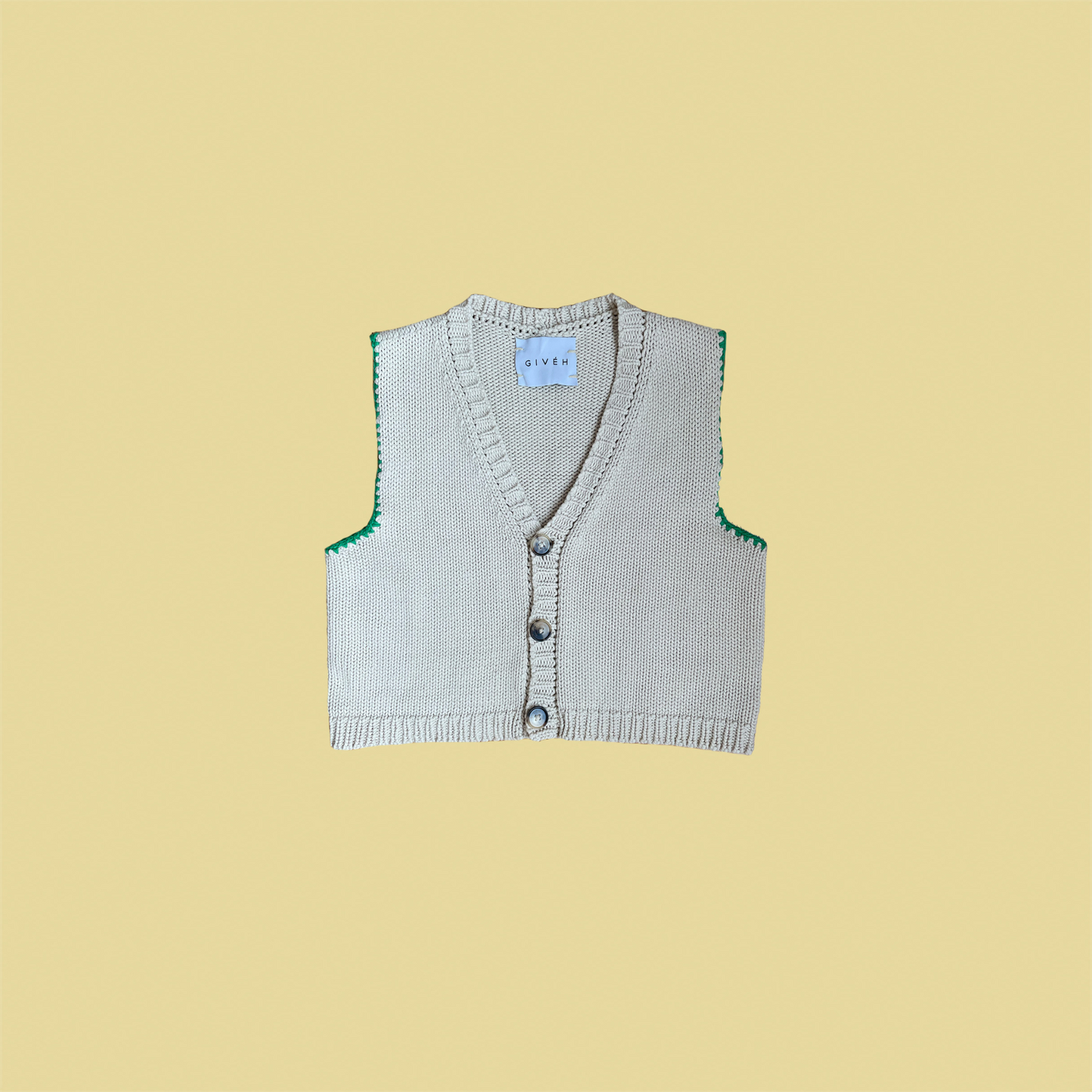 givéh knitwear handmade by female artisans in iran using only natural and recycled fibres. contemporary knitwear for cool people. cream vesty vest, cream and green knit vest with three natural horn buttons, made of cotton and recycled polyamide yarn, handcrocheted edges. spring summer 2025 collection.
