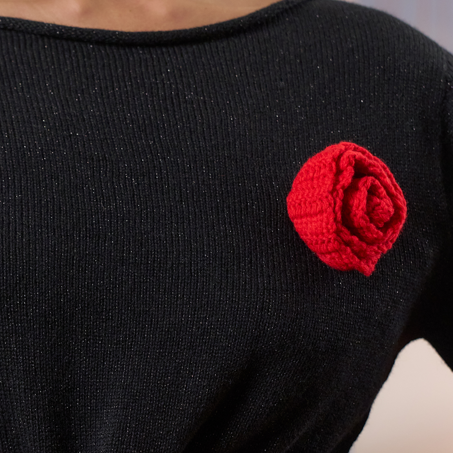 givéh knitwear handmade by female artisans in iran using only natural and recycled fibres. contemporary knitwear for cool people. black dress with red hand crocheted flower. made of merino wool. fall 2025 collection.