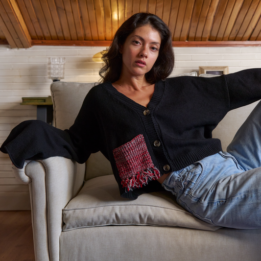 givéh knitwear handmade by female artisans in iran using only natural and recycled fibres. contemporary knitwear for cool people. black cardigan with red/black gradient fringe pocket. 3 natural horn buttons. 100% merino wool. fall 2025 collection.
