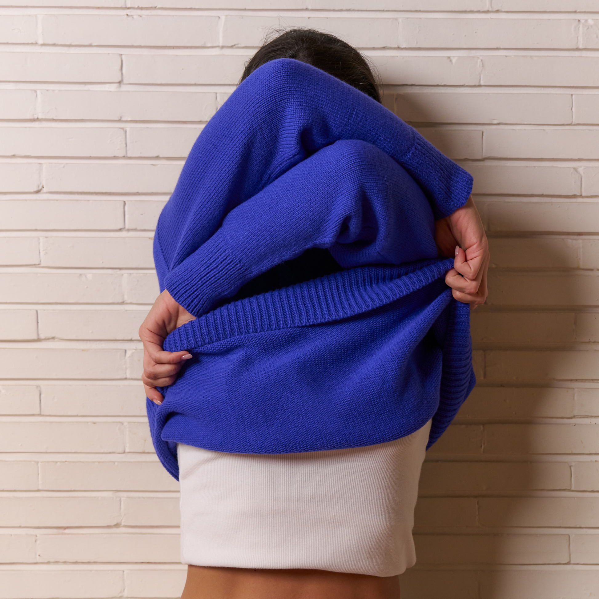Person wearing a blue sweater against a light brick wall.
givéh knitwear handmade by female artisans in iran using only natural and recycled fibres. contemporary knitwear for cool people. blue unisex crewneck sweater. 100% merino wool. fall 2025 collection.
