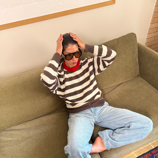 Person wearing a striped sweater and sunglasses sitting on a green couch.
givéh knitwear handmade by female artisans in iran using only natural and recycled fibres. contemporary knitwear for cool people. brown and cream striped unisex sweater with red crew neckline. 100% merino wool. fall 2025 collection.